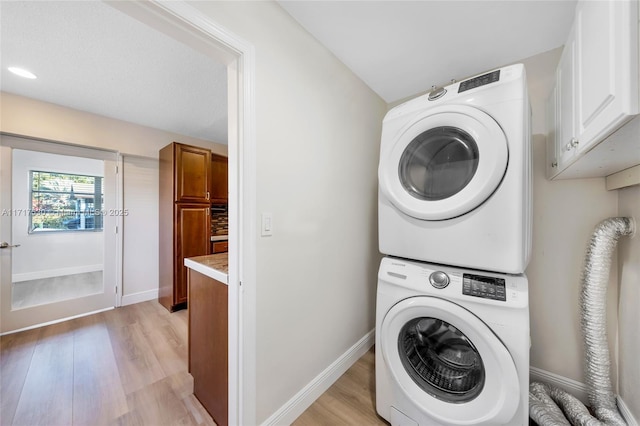 washroom featuring stacked washer / drying machine, light hardwood / wood-style floors, and cabinets