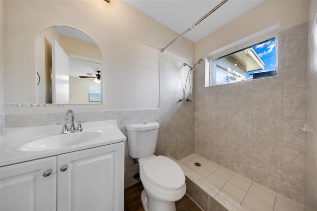 bathroom with vanity, ceiling fan, toilet, tiled shower, and tile walls