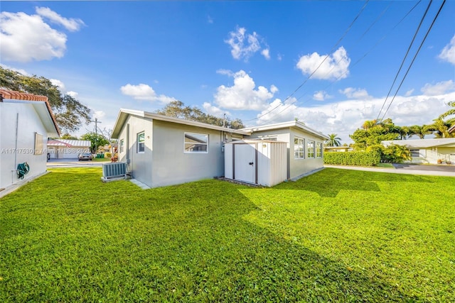 rear view of property with a yard, central AC, and a storage shed