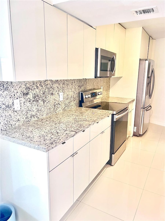 kitchen featuring backsplash, white cabinets, light tile patterned floors, appliances with stainless steel finishes, and light stone counters