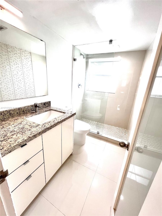 bathroom featuring tile patterned flooring, a tile shower, vanity, and toilet