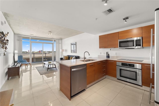 kitchen with sink, light tile patterned floors, a wall of windows, stainless steel appliances, and kitchen peninsula