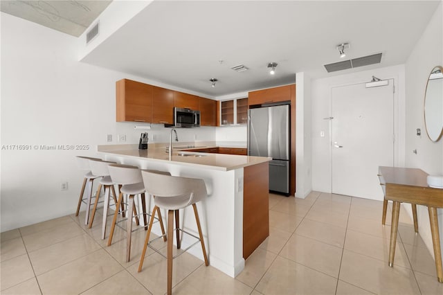 kitchen with light tile patterned flooring, appliances with stainless steel finishes, sink, a kitchen breakfast bar, and kitchen peninsula
