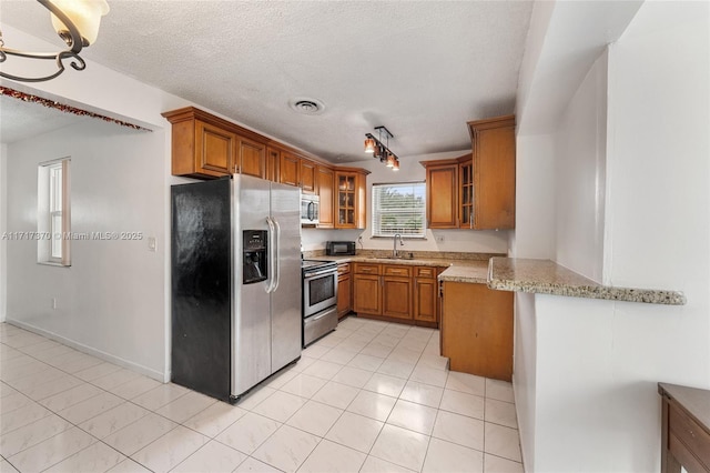 kitchen with kitchen peninsula, light stone counters, a textured ceiling, stainless steel appliances, and sink