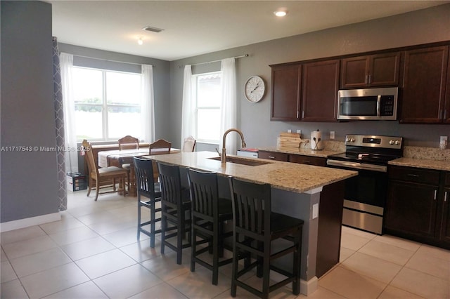 kitchen with a kitchen breakfast bar, sink, an island with sink, light stone counters, and stainless steel appliances