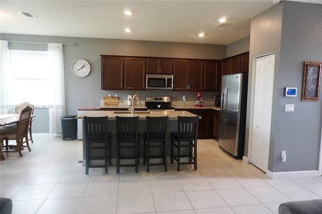 kitchen featuring dark brown cabinetry, sink, stainless steel appliances, a kitchen breakfast bar, and a kitchen island with sink