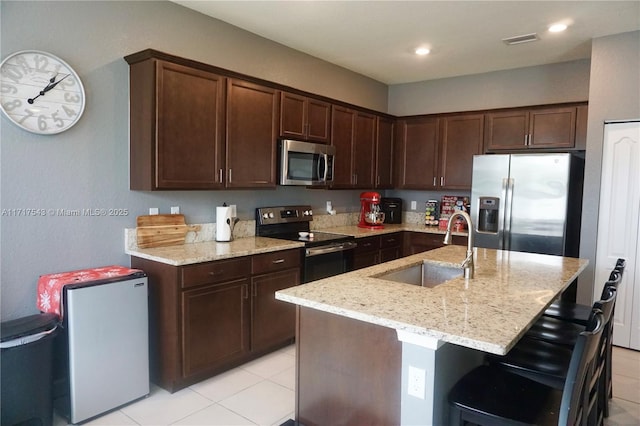 kitchen with an island with sink, stainless steel appliances, light stone counters, and sink