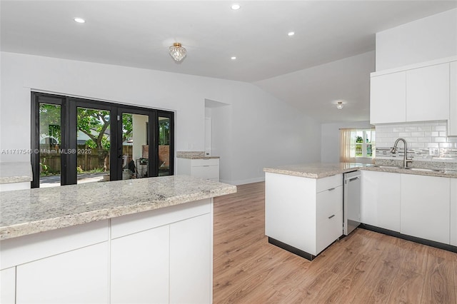 kitchen featuring kitchen peninsula, backsplash, stainless steel dishwasher, white cabinets, and lofted ceiling