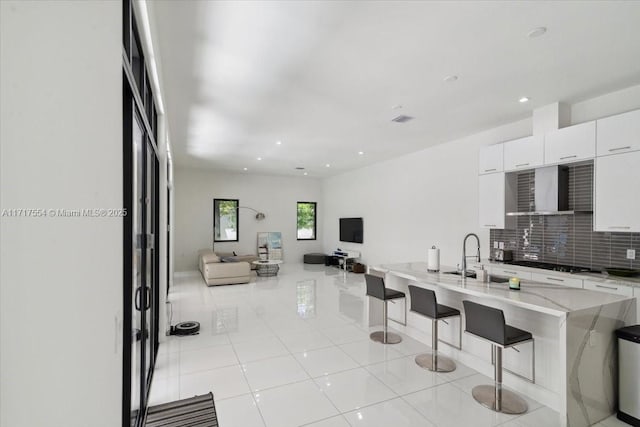 kitchen with backsplash, black gas stovetop, wall chimney range hood, white cabinetry, and a breakfast bar area