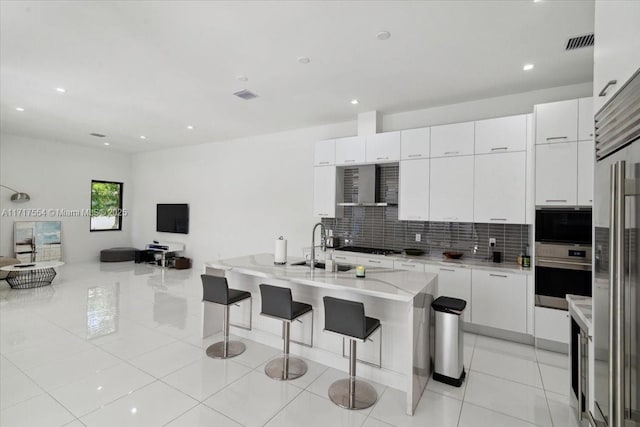 kitchen with white cabinets, decorative backsplash, wall chimney exhaust hood, appliances with stainless steel finishes, and a breakfast bar area