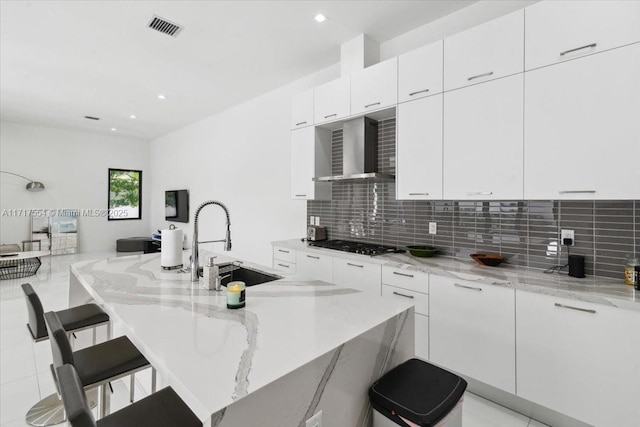 kitchen featuring wall chimney exhaust hood, a kitchen breakfast bar, white cabinets, and light stone countertops