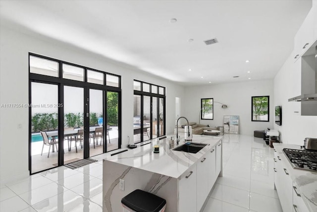 kitchen featuring light stone countertops, sink, stainless steel gas cooktop, a large island with sink, and white cabinets