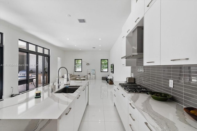 kitchen featuring light stone countertops, sink, wall chimney range hood, stainless steel gas stovetop, and white cabinets