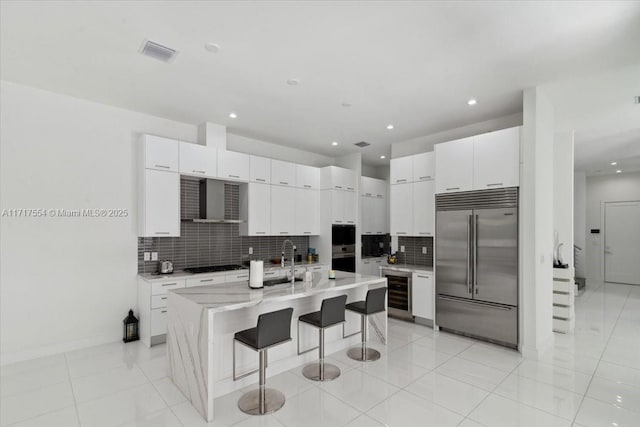 kitchen with a center island with sink, stainless steel built in fridge, white cabinetry, wine cooler, and a breakfast bar area