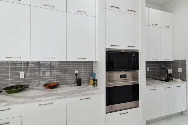 kitchen featuring decorative backsplash, light stone counters, stainless steel oven, black microwave, and white cabinets