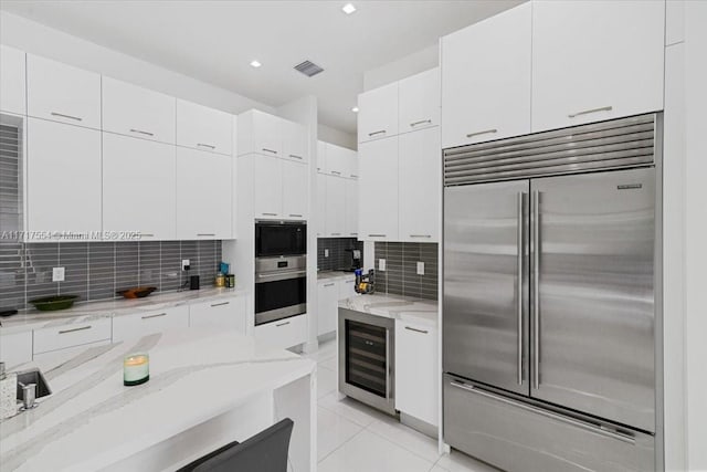 kitchen featuring light stone countertops, beverage cooler, backsplash, built in appliances, and white cabinets