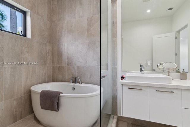 bathroom with vanity, tile walls, and a tub