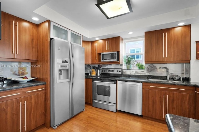 kitchen with decorative backsplash, stainless steel appliances, sink, dark stone countertops, and light hardwood / wood-style floors