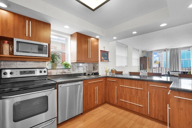 kitchen with sink, light hardwood / wood-style flooring, backsplash, dark stone countertops, and appliances with stainless steel finishes