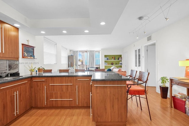 kitchen featuring a breakfast bar, dark stone counters, sink, light hardwood / wood-style floors, and kitchen peninsula