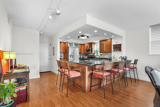 kitchen featuring kitchen peninsula, a kitchen bar, tasteful backsplash, stainless steel appliances, and light hardwood / wood-style floors