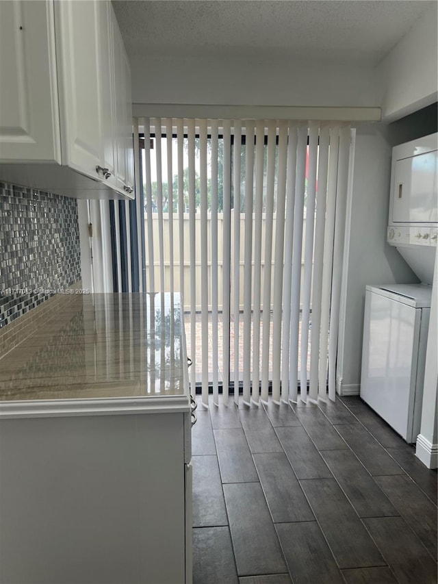 kitchen featuring white cabinets, stacked washing maching and dryer, backsplash, and a textured ceiling