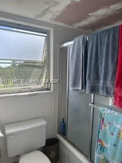 bathroom with shower / bath combination with glass door, toilet, and a wealth of natural light