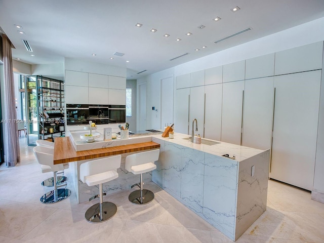 kitchen featuring white cabinets, a kitchen breakfast bar, sink, light stone countertops, and a large island