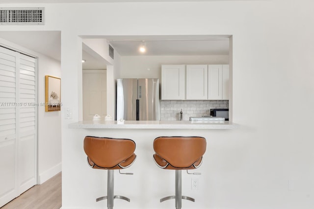 kitchen with decorative backsplash, light wood-type flooring, white cabinetry, a breakfast bar area, and stainless steel refrigerator