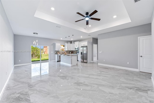 unfurnished living room with ceiling fan and a raised ceiling