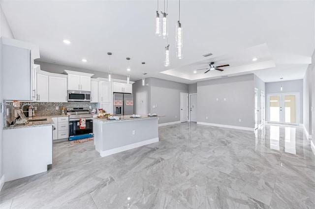 kitchen featuring stainless steel appliances, a kitchen island, decorative light fixtures, a tray ceiling, and white cabinets