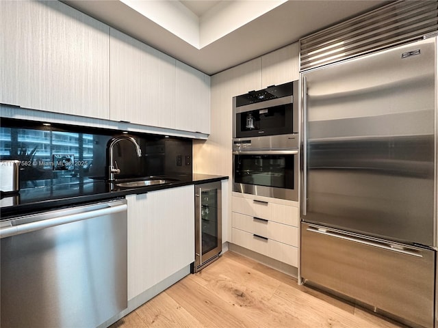 kitchen with appliances with stainless steel finishes, tasteful backsplash, sink, wine cooler, and light hardwood / wood-style floors