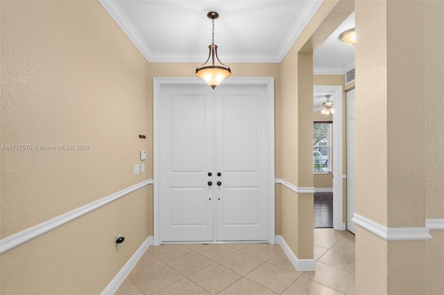 tiled foyer with ceiling fan and crown molding