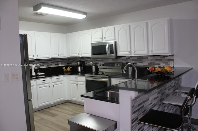 kitchen featuring kitchen peninsula, decorative backsplash, white cabinets, and appliances with stainless steel finishes