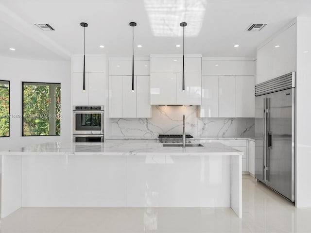 kitchen with light stone counters, white cabinets, hanging light fixtures, and appliances with stainless steel finishes