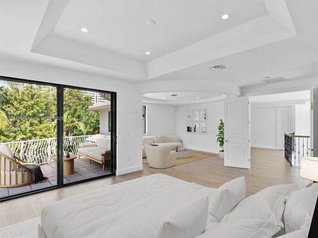 bedroom with access to exterior, a raised ceiling, and hardwood / wood-style flooring