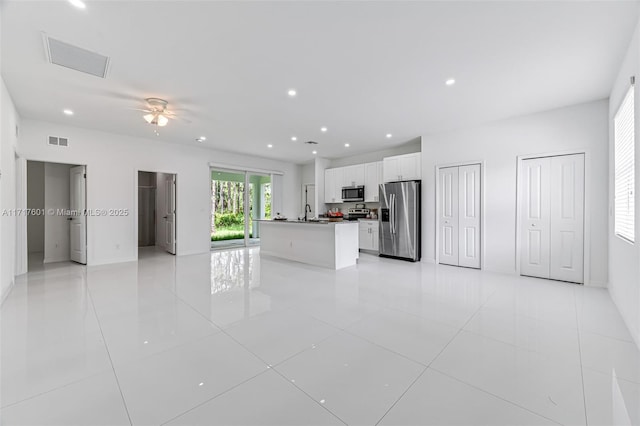 interior space with stainless steel appliances, ceiling fan, a center island with sink, white cabinetry, and light tile patterned flooring