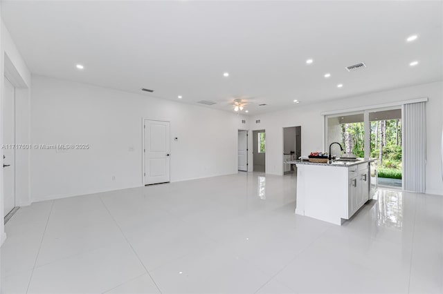 kitchen with ceiling fan, sink, light tile patterned floors, a kitchen island with sink, and white cabinets