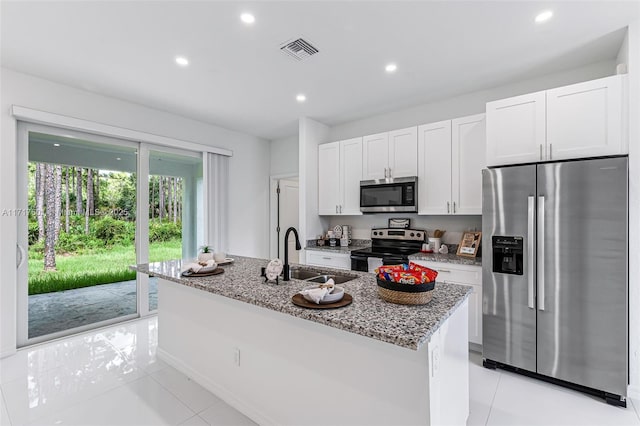 kitchen with light stone countertops, appliances with stainless steel finishes, a kitchen island with sink, sink, and white cabinetry