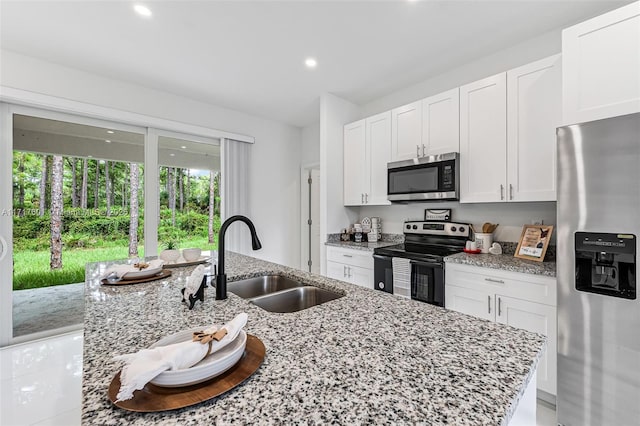 kitchen featuring light stone counters, stainless steel appliances, sink, white cabinetry, and an island with sink