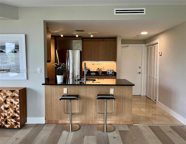 kitchen with a breakfast bar, kitchen peninsula, sink, and stainless steel refrigerator