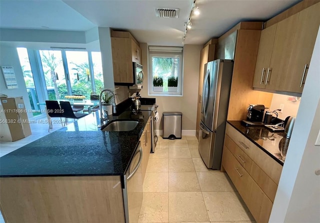 kitchen with a wealth of natural light, sink, stainless steel appliances, dark stone counters, and light tile patterned flooring