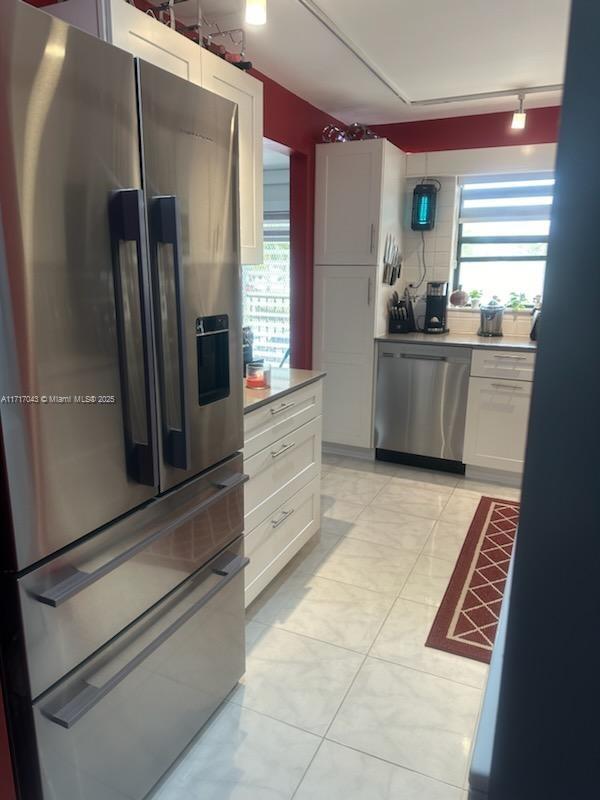 kitchen featuring decorative backsplash, white cabinetry, light tile patterned floors, and stainless steel appliances