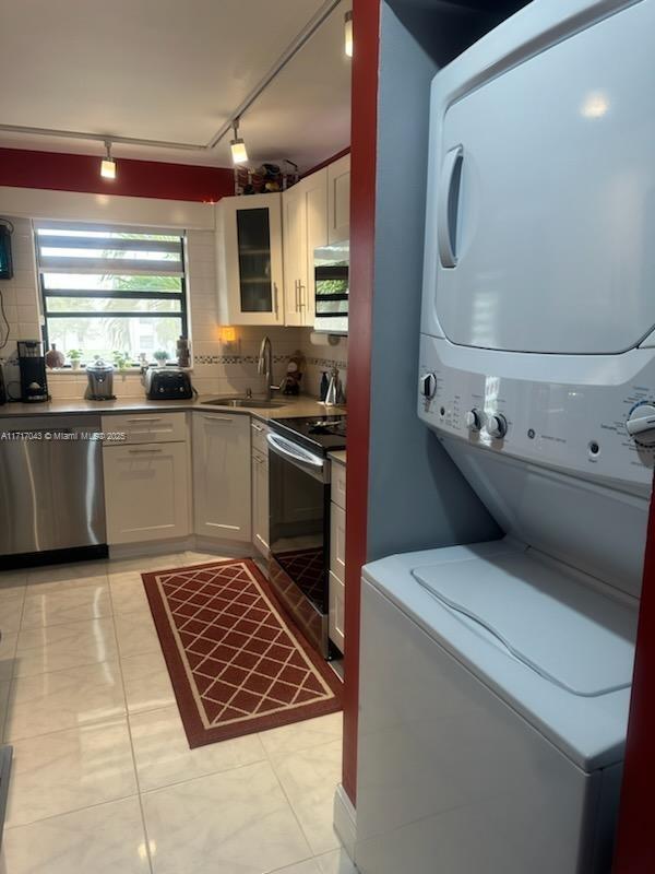 kitchen featuring white cabinets, stainless steel appliances, sink, stacked washer and clothes dryer, and light tile patterned flooring