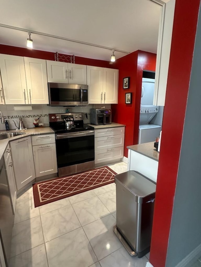 kitchen featuring sink, white cabinets, stacked washer / drying machine, and stainless steel appliances