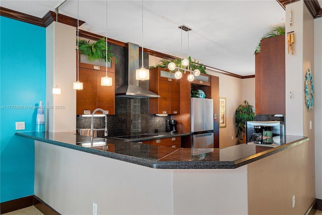 kitchen featuring pendant lighting, wall chimney range hood, kitchen peninsula, and stainless steel refrigerator