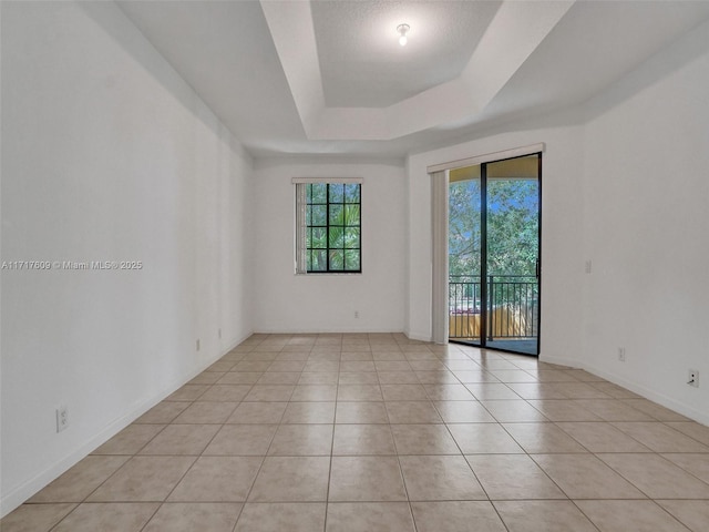 empty room with a raised ceiling and light tile patterned flooring