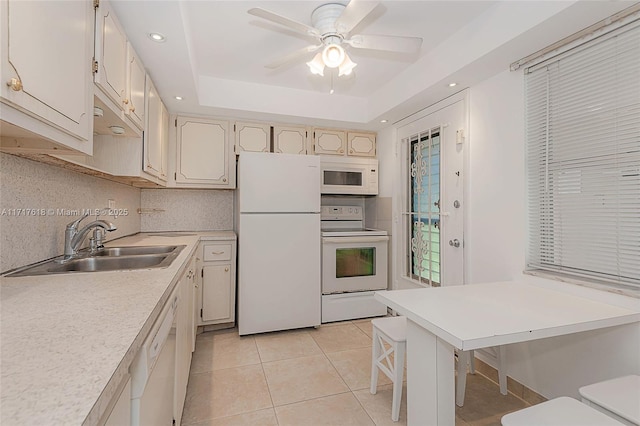 kitchen with white appliances, a raised ceiling, sink, light tile patterned flooring, and a breakfast bar area