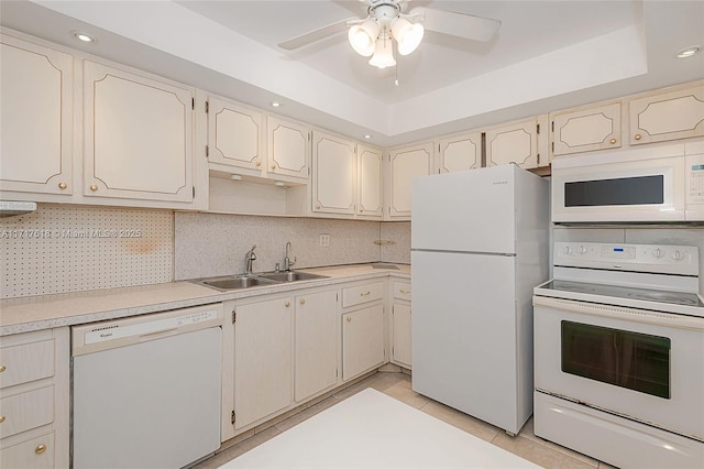 kitchen with sink, tasteful backsplash, white appliances, a tray ceiling, and light tile patterned floors