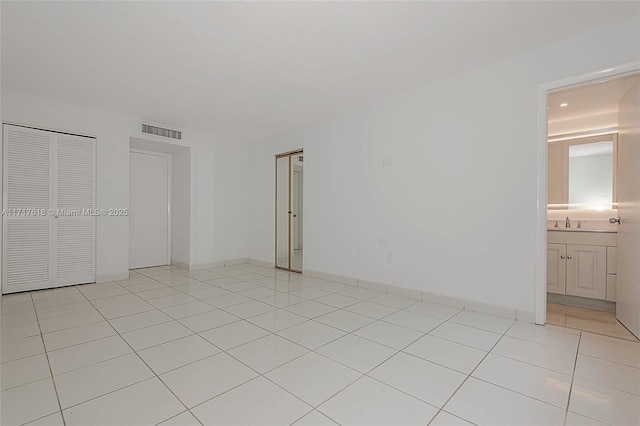 unfurnished bedroom with ensuite bath, a closet, light tile patterned floors, and sink